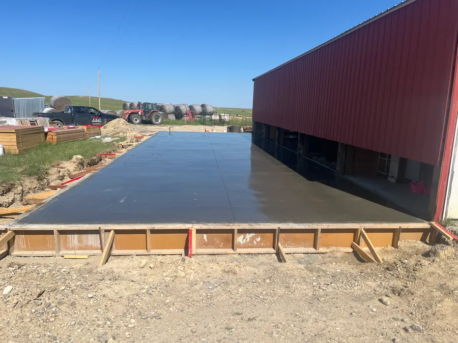 Freshly poured concrete slab beside the existing red steel building