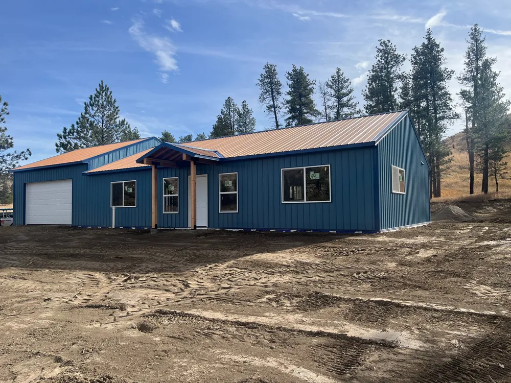 Completed custom stick-framed home with blue siding and red metal roof near Billings, Montana
