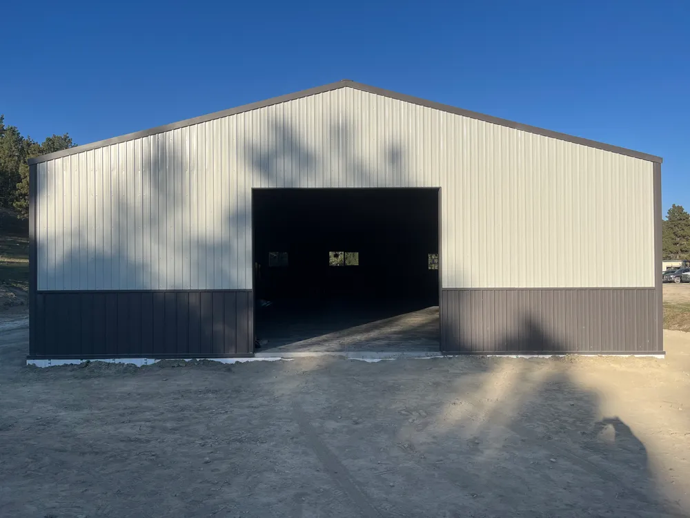Gray stick-framed shop home with a full-height overhead door on a rural Montana property